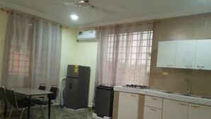 A compact kitchen with a dining table, chairs, a refrigerator, a sink, and a ceiling fan. - Charming 1-bedroom apartment in Tema with AC (Tema)