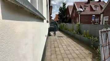 Ein schmaler gepflasterter Weg führt zu einem Wohngebäude mit weißer Fassade und Ziegelverkleidung.