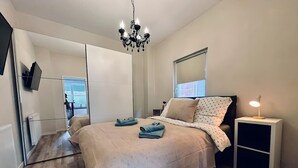A bedroom with a bed, a nightstand with a lamp, a mirror, and a view of the outside. - Bentheimpje - Center & Charming (Bad Bentheim)