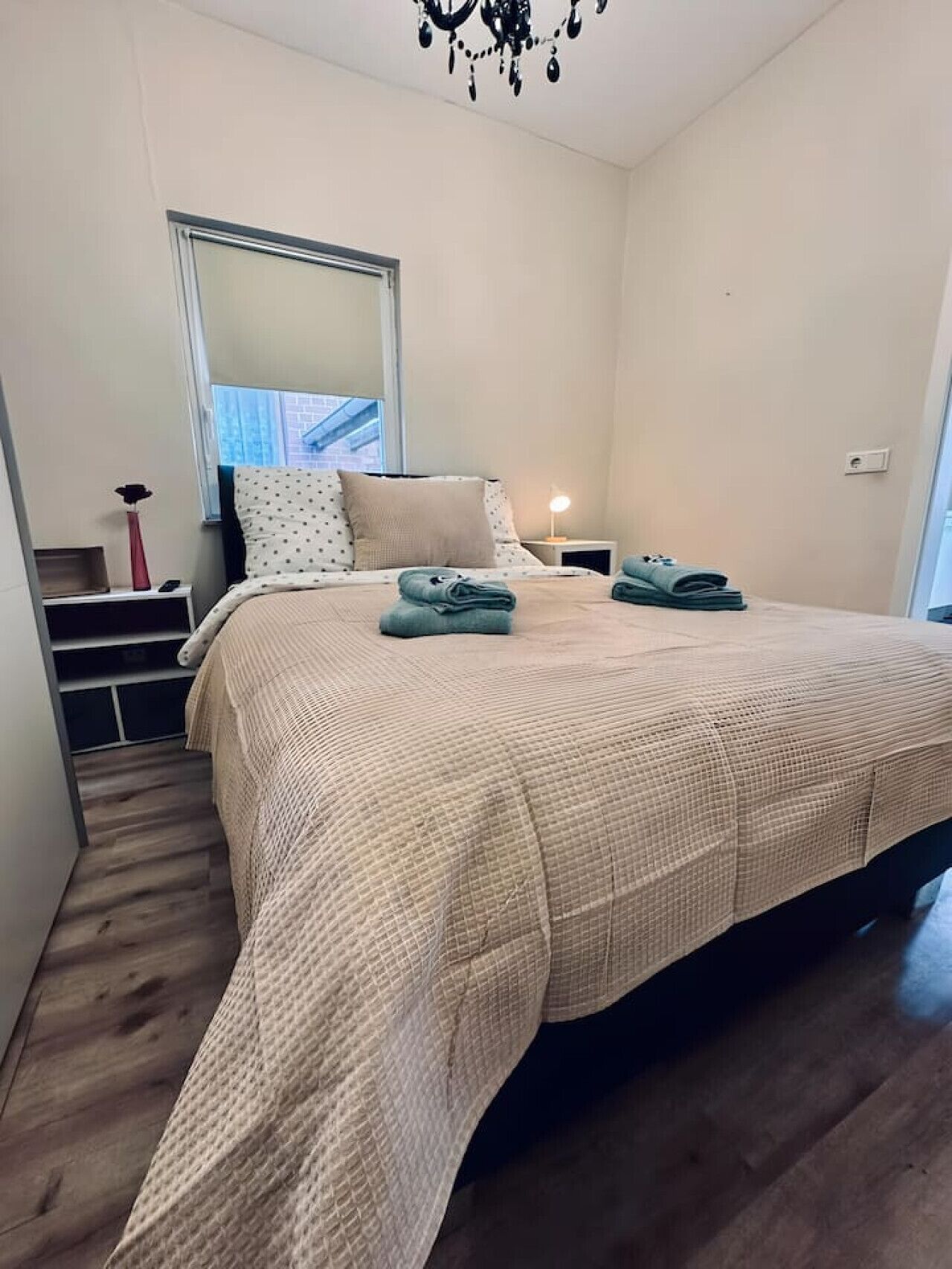 A bedroom with a large bed, a nightstand, a lamp, and a window with a view of a building.