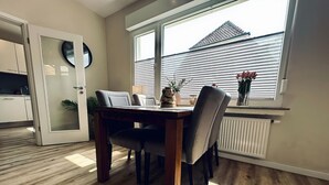 A dining area with a wooden table and chairs, a large window with blinds, and a view of a building outside. - Bentheimpje - Center & Charming (Bad Bentheim)