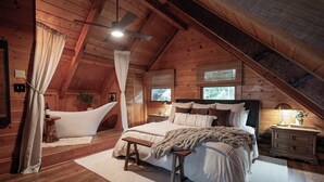 Un dormitorio acogedor en el ático, con techo abovedado, cama grande, bañera y banco de madera.