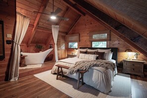 Ein gemütliches Schlafzimmer im Dachgeschoss mit gewölbter Decke, einem großen Bett, einer Badewanne und einer hölzernen Sitzbank.