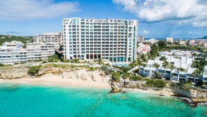 Un hotel grande con varios pisos, una playa y aguas turquesas cristalinas.