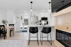 A modern kitchen with white cabinets, a black refrigerator, and a wooden dining area with two black chairs.