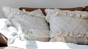 Een bed met twee grote, gestructureerde kussens en een plaids.