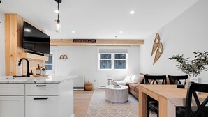Een moderne keuken met witte kasten, een ingebouwde televisie en een eethoek met een houten tafel en stoelen.