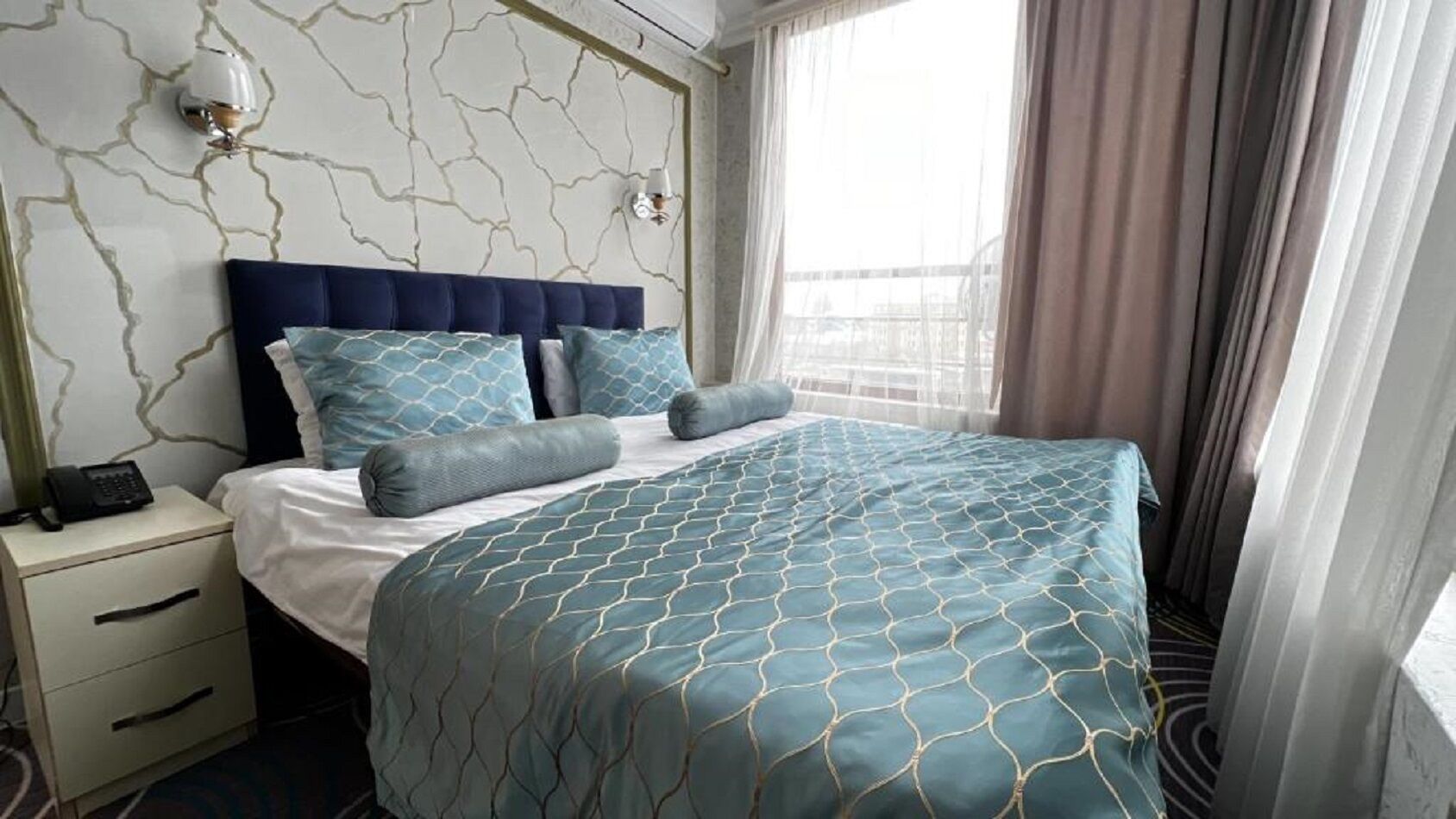 Een hotelkamer met een bed, nachtkastje, telefoon en een raam met gordijnen.