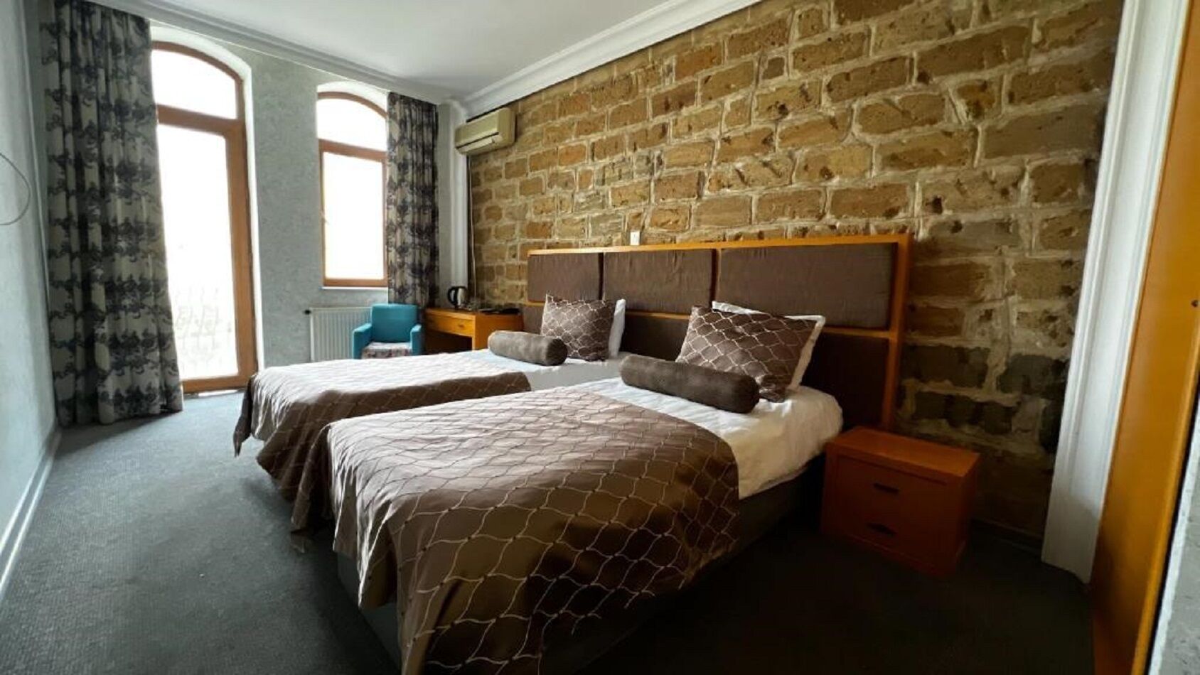 Een slaapkamer met twee bedden, een bakstenen muur, een raam en een nachtkastje.