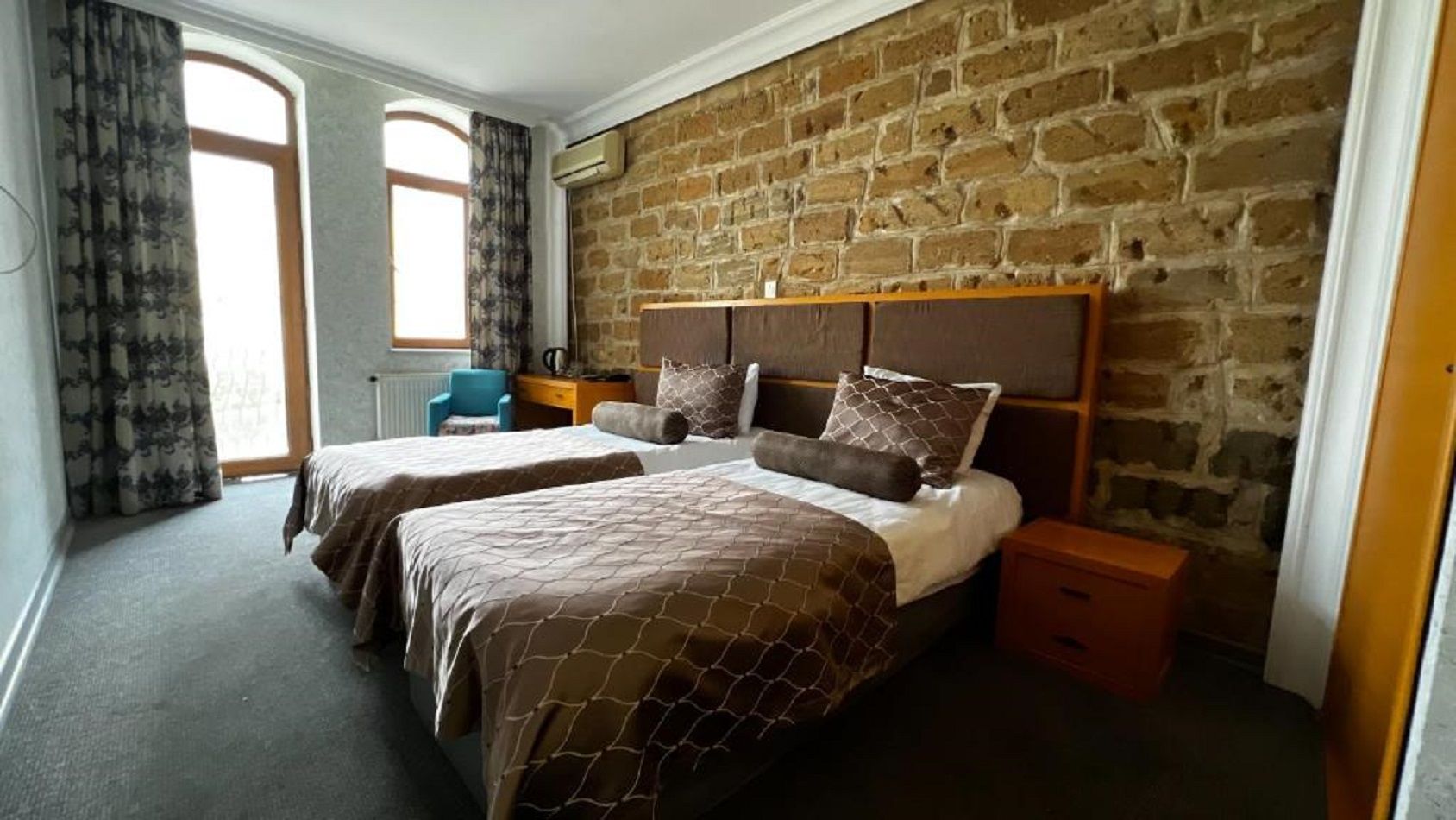Une chambre avec deux lits, un mur en briques, une fenêtre et une table de chevet.