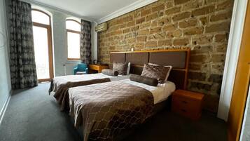 Une chambre avec deux lits, un mur en briques, une fenêtre et une table de chevet.