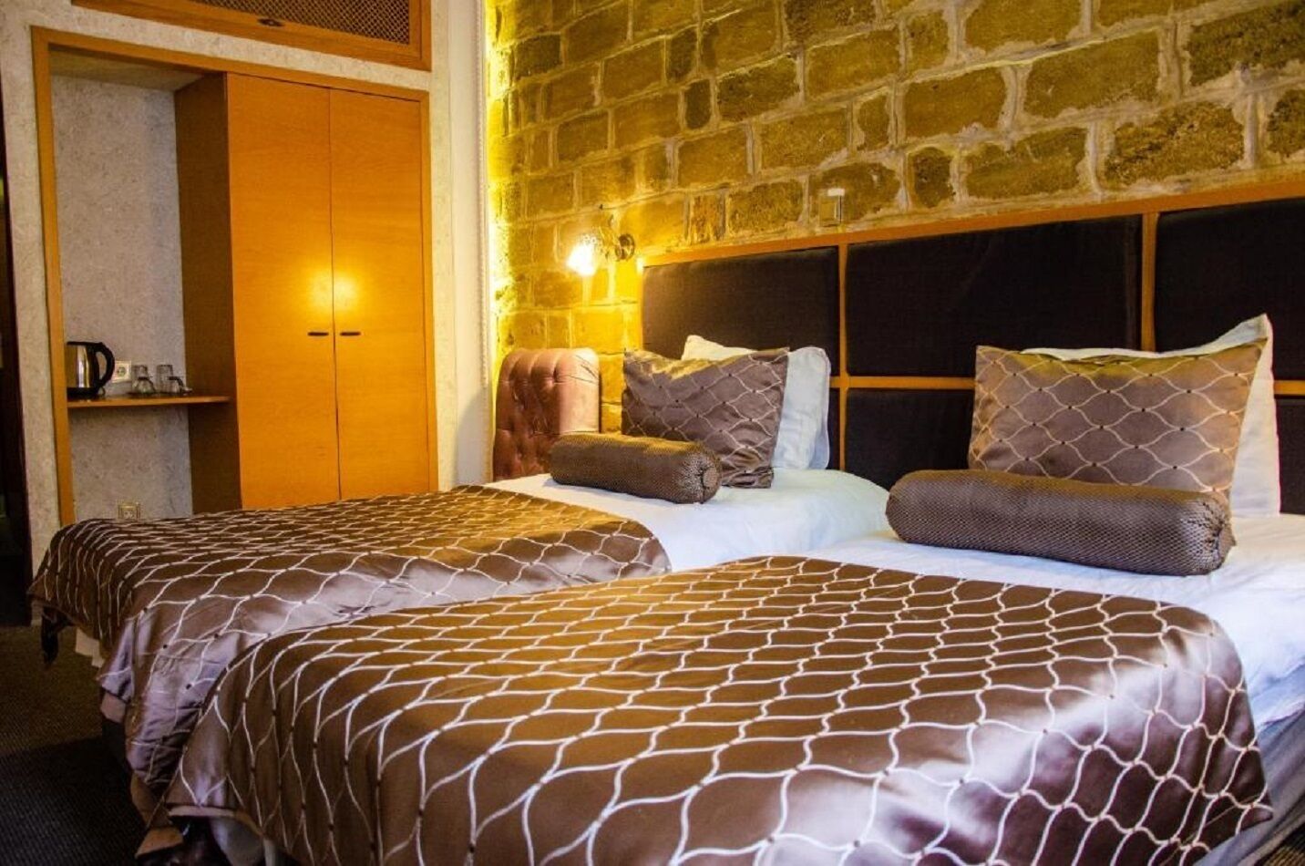 Een hotelkamer met twee bedden, een bakstenen muur en een houten garderobe.