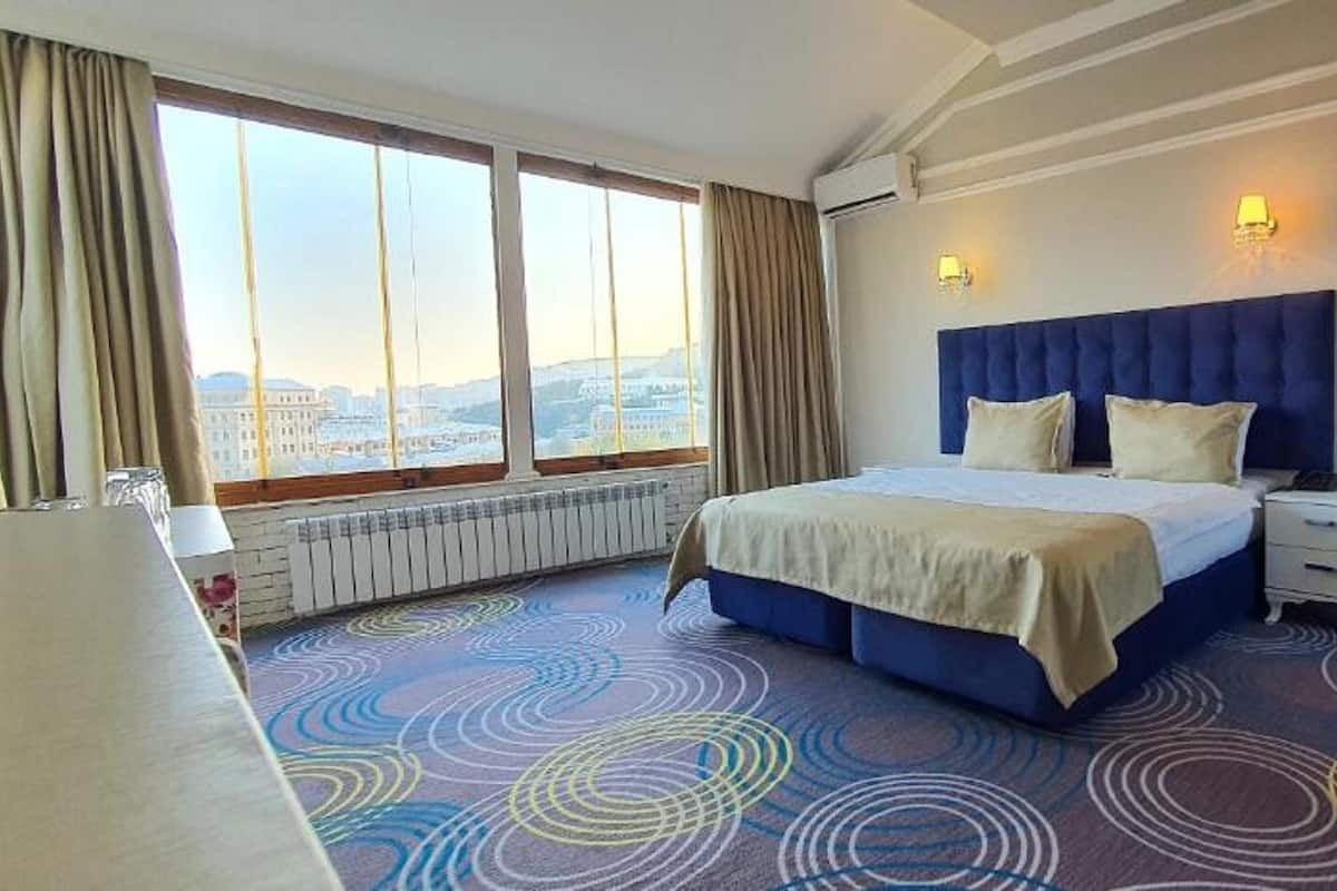 Une chambre d’hôtel avec un grand lit, une table de chevet, une fenêtre avec des rideaux et une vue sur la ville.