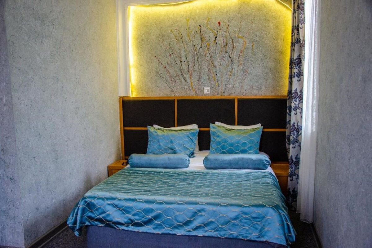 Een bed met een geborduurde blauwe dekbedovertrek en passende kussens, een houten hoofdbord en een wandlamp.
