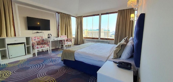 A hotel room with a bed, a desk, a chair, a TV, and a view of the city.