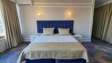 Une chambre d’hôtel avec un grand lit, deux tables de chevet, une tête de lit et une fenêtre avec des rideaux.