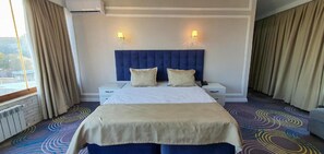 Une chambre d’hôtel avec un grand lit, deux tables de chevet, une tête de lit et une fenêtre avec des rideaux.