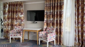 Een kamer met twee fauteuils met bloemenprint, een klein witte tafel en een flatscreen televisie aan de muur.