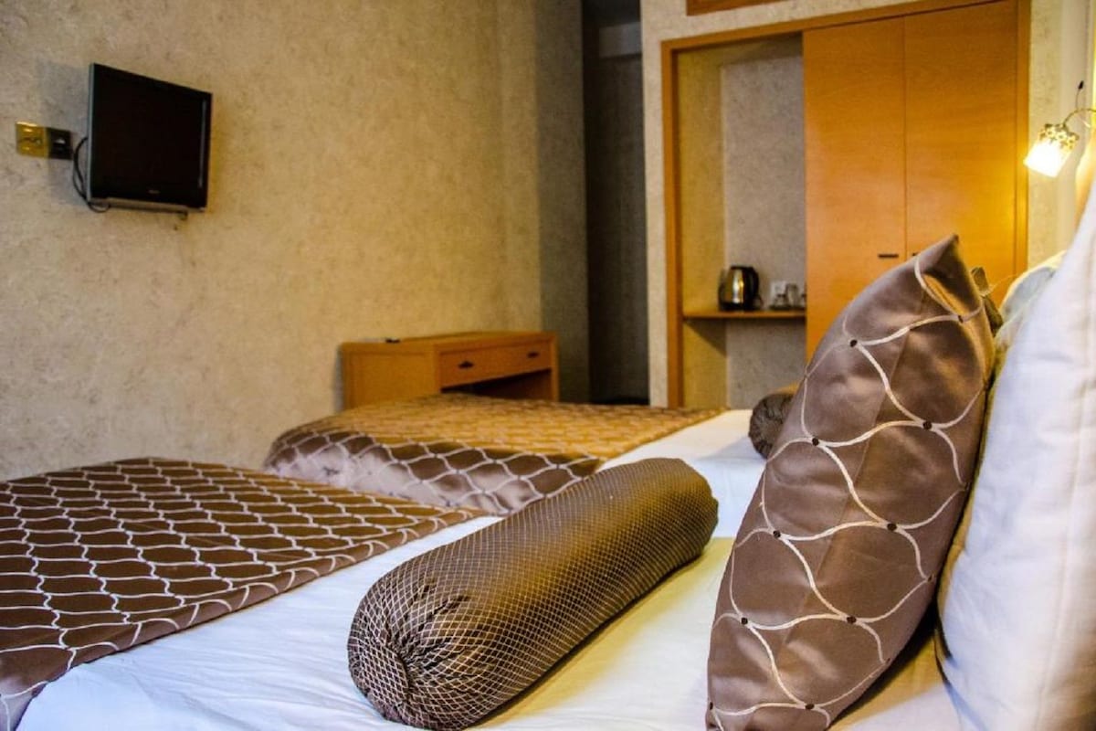 Hotellihuone, jossa on kaksi sänkyä, seinälle asennettu televisio ja puinen vaatekaappi.