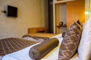 Une chambre d’hôtel avec deux lits, un téléviseur fixé au mur et une armoire en bois.