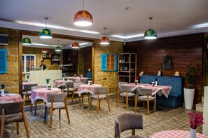 Een restaurant met meerdere tafels en stoelen, een bar en een zithoek met een blauwe bank.
