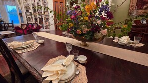 A dining room with a long table set for a meal, surrounded by bookshelves and a large floral arrangement. - Baer House Inn (Vicksburg)