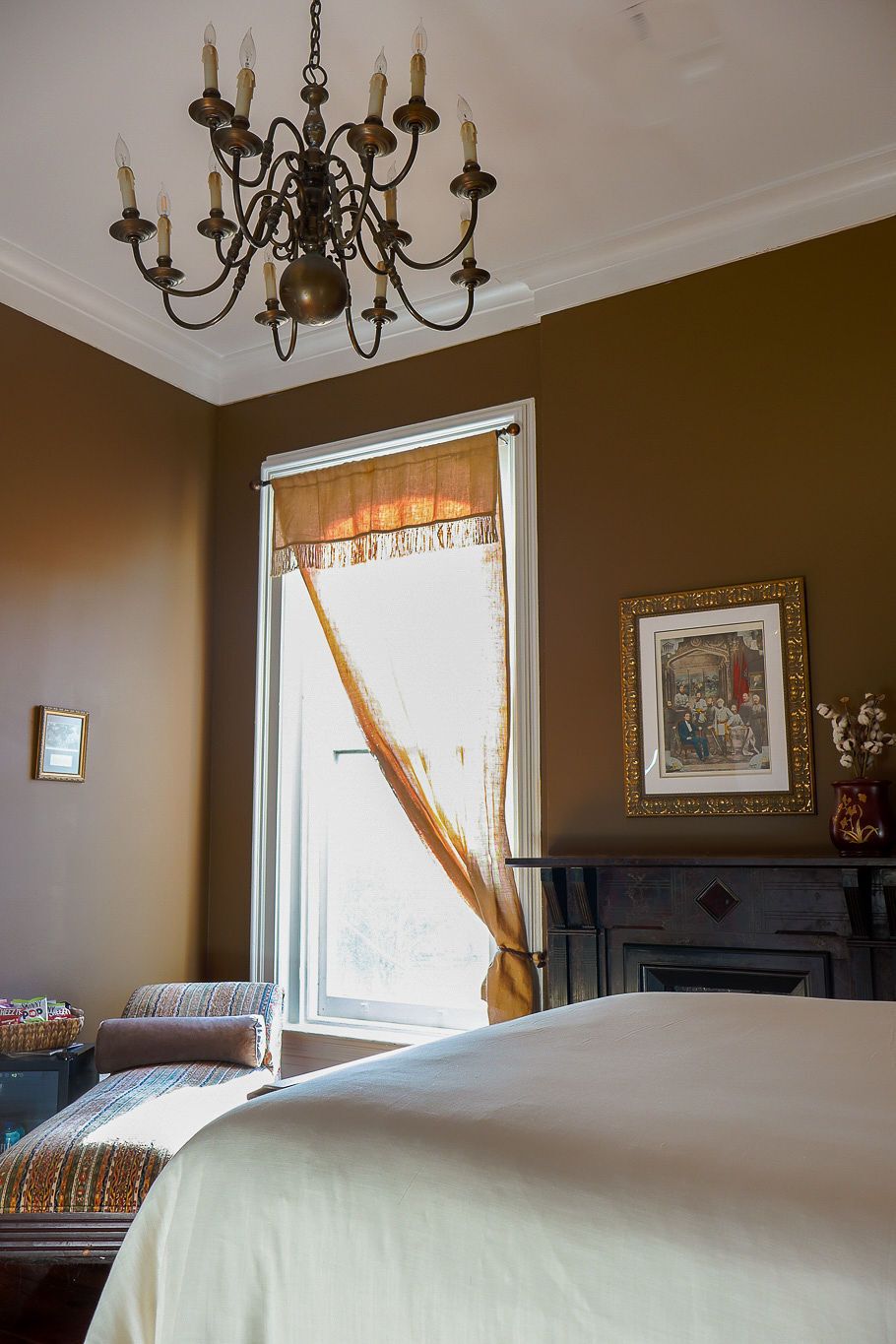 A bedroom with a large bed, a chandelier, a fireplace, and a window with curtains.