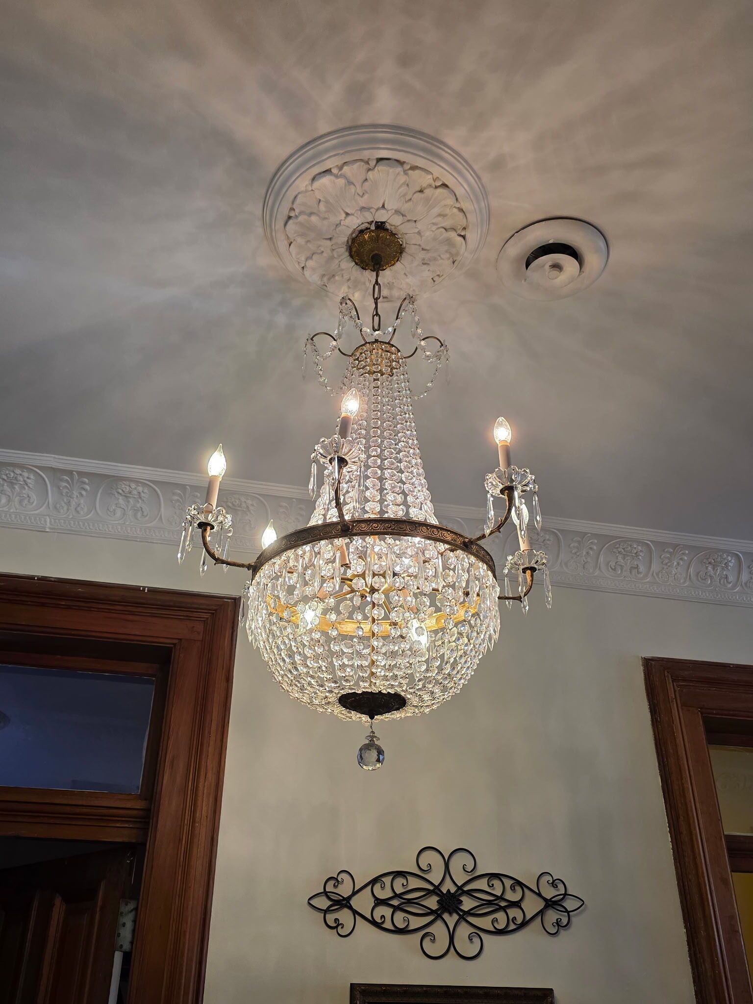 Un candelabro con varias luces, techo decorativo y un adorno metálico en la pared.