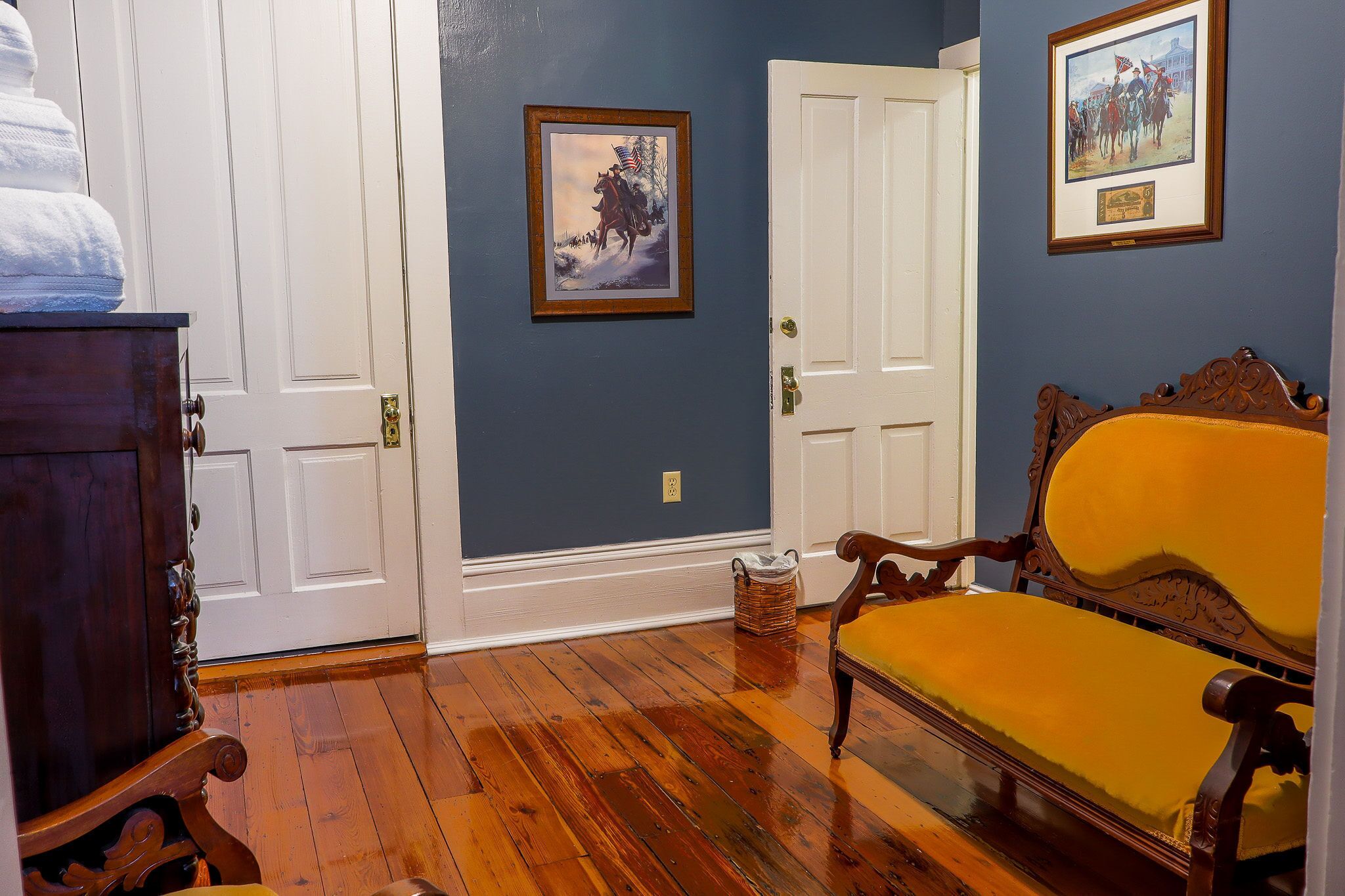 A room with wooden flooring, a yellow upholstered bench, a wooden cabinet, and two doors.