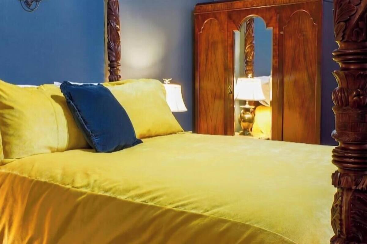 A bed with yellow bedding, a blue pillow, and a wooden headboard.