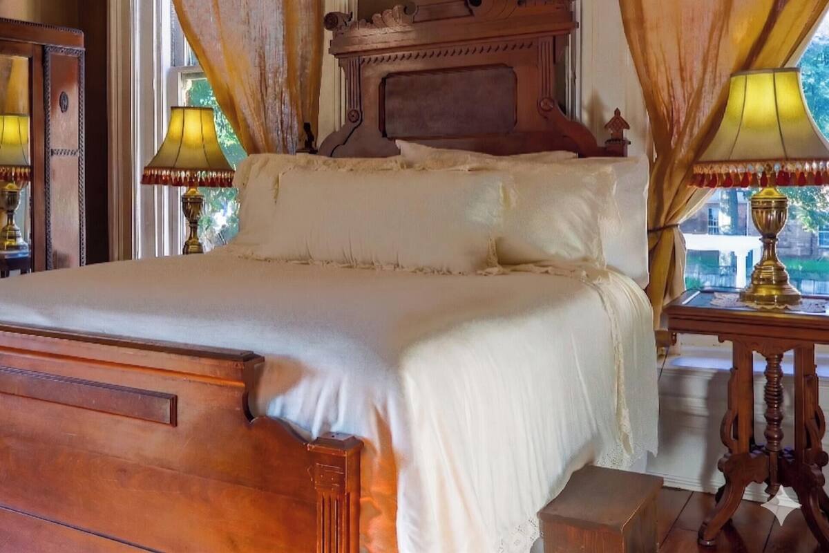A classic four-poster bed with a wooden headboard, white linens, and two bedside lamps.