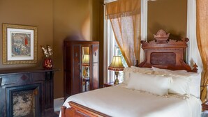 A bedroom with a bed, a wooden dresser, a mirror, a fireplace, and a window with curtains. - Baer House Inn (Vicksburg)