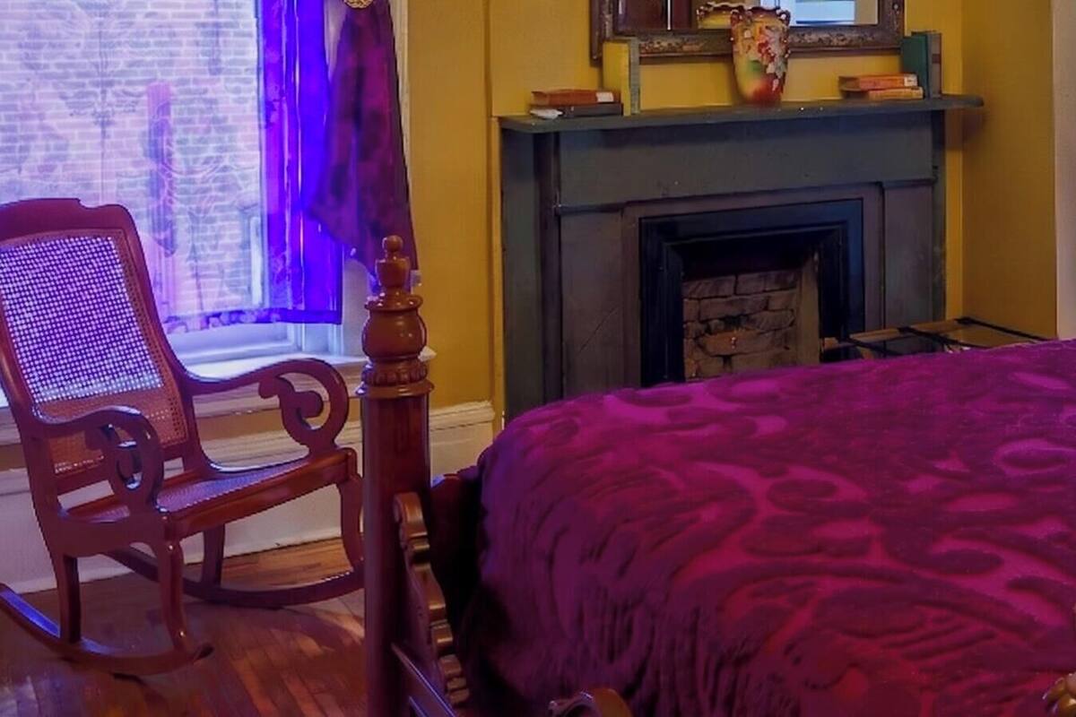 A bedroom with a bed, a fireplace, a chair, and a window with curtains.