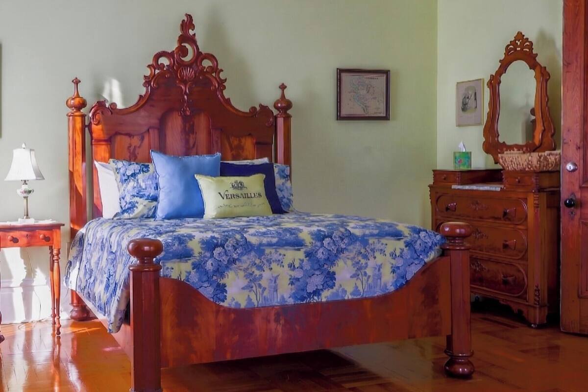 A wooden bed with a floral bedspread, a nightstand with a lamp, and a dresser with a mirror.