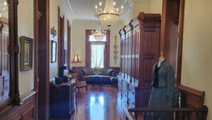 A spacious hallway with polished wooden floors, a grand chandelier, and a mannequin dressed in denim. - Baer House Inn (Vicksburg)