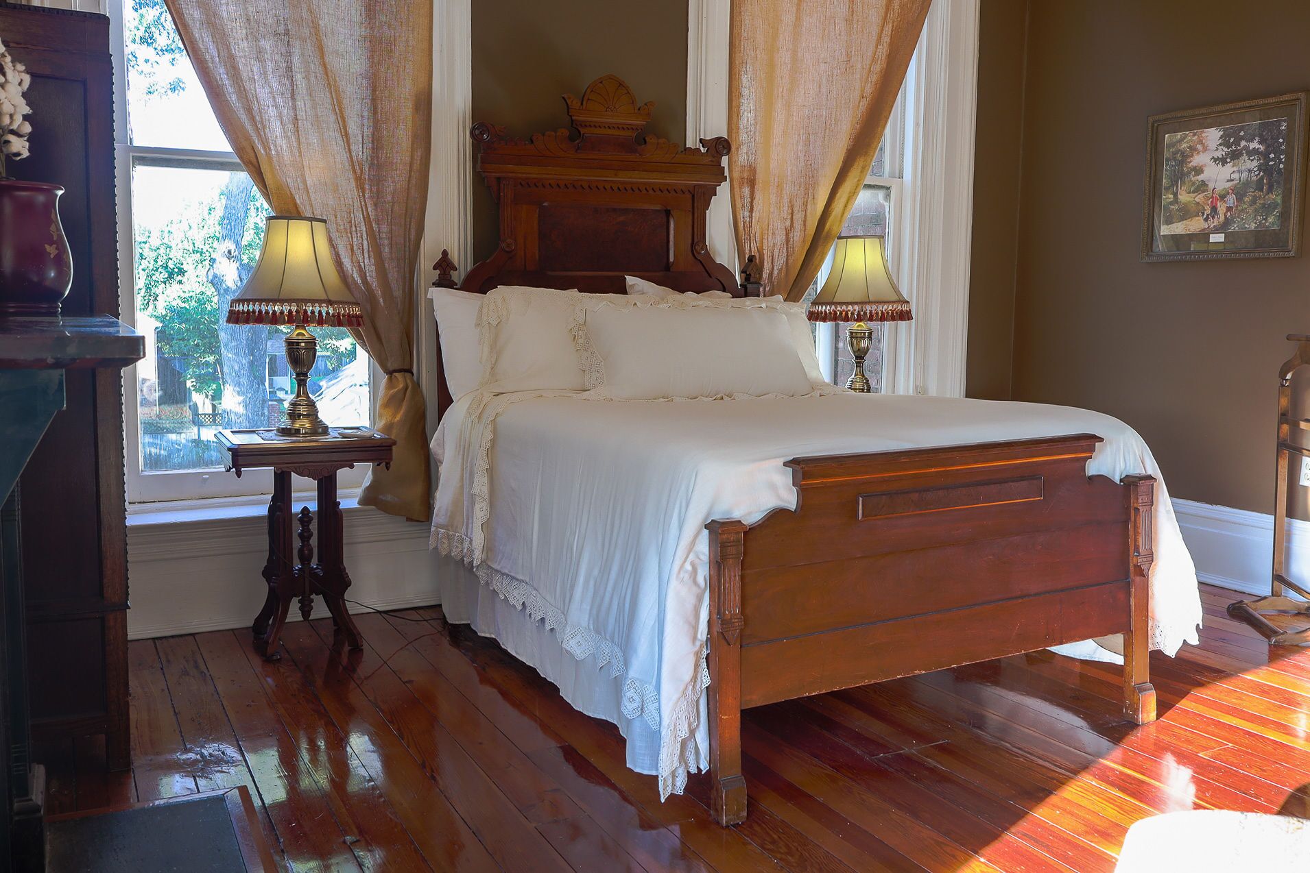 A traditional wooden bed with white linens, two bedside tables with lamps, and a window with curtains.