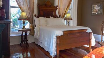 A traditional wooden bed with white linens, two bedside tables with lamps, and a window with curtains.