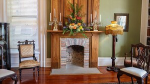 A room with a brick fireplace, a floral arrangement, and two chairs. - Baer House Inn (Vicksburg)