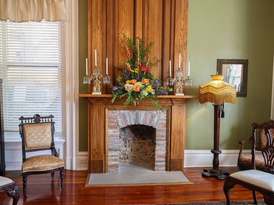 A room with a brick fireplace, a floral arrangement, and two chairs.