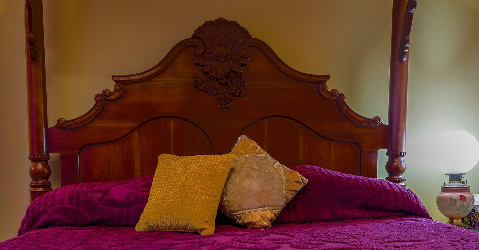A four-poster bed with a wooden headboard, a purple bedspread, and two pillows.