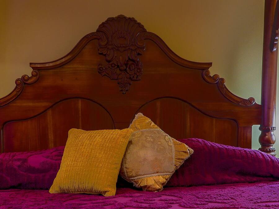 A four-poster bed with a wooden headboard, a purple bedspread, and two pillows.