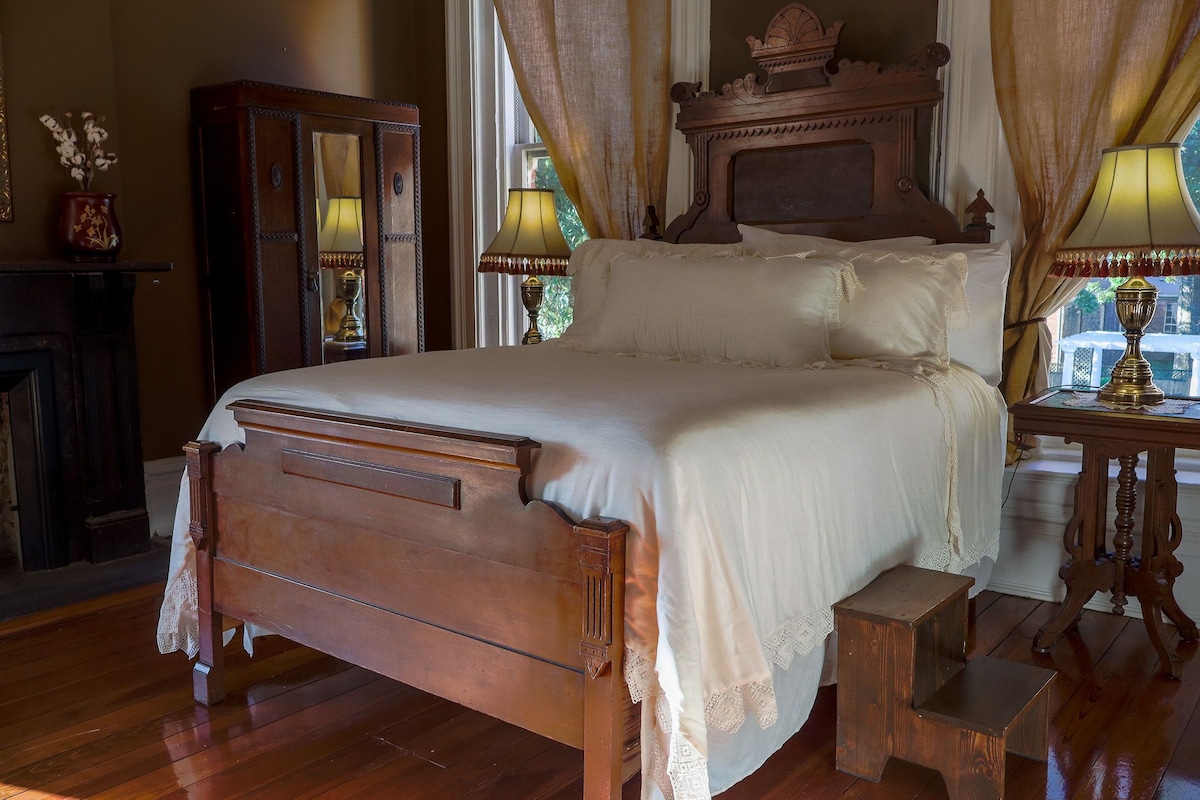 Een klassiek houten bed met voeteneind, een nachtkastje met lamp en een spiegel.
