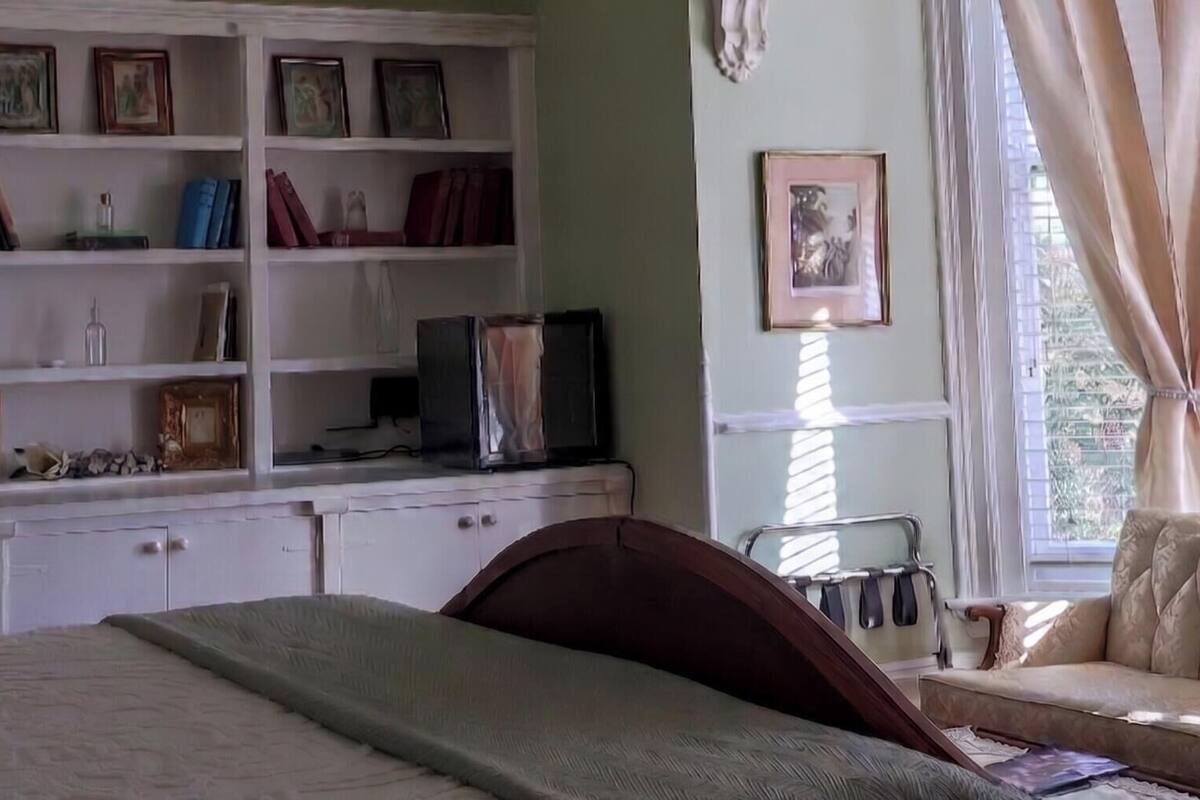 A bedroom with a bed, a white wardrobe, a television, and a window with curtains.