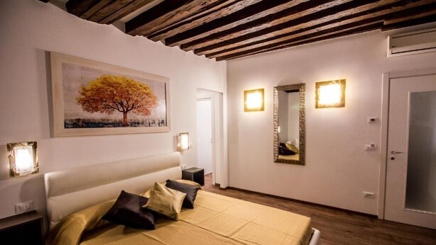 A bedroom with a bed, bedside lamps, a painting, and a mirror. - GOLDEN SUITE (Venezia)