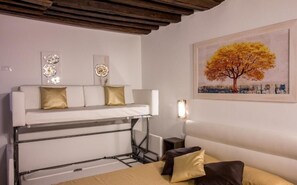 A compact room with a bunk bed, a bedside table, a lamp, and a painting of a tree. - GOLDEN SUITE (Venezia)