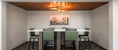 A dining area with a white table, four green chairs, a wooden ceiling, and a patterned floor.