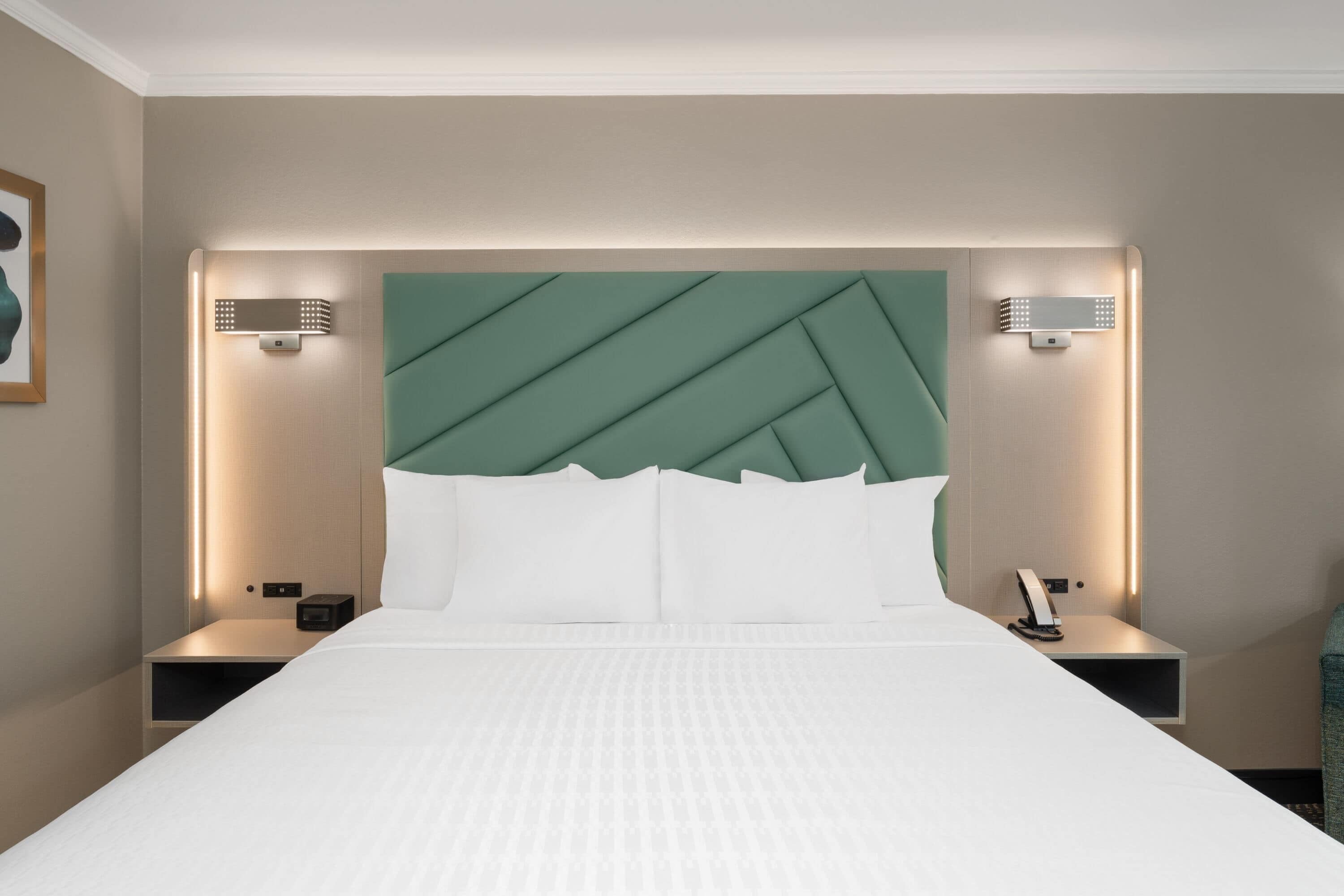Une chambre d’hôtel avec un grand lit, deux tables de chevet, une tête de lit verte et des lampes fixées au mur.
