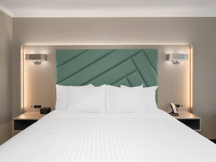 Une chambre d’hôtel avec un grand lit, deux tables de chevet, une tête de lit verte et des lampes fixées au mur.