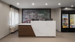 Un comptoir d’accueil avec un plateau en marbre blanc et un socle en bois, une grande affiche représentant un pont, et un réfrigérateur rempli de boissons.