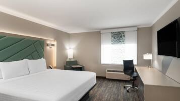 Ein Hotelzimmer mit Bett, Schreibtisch, Stuhl, Fernseher, einem Fenster mit Jalousien und einer Wandleuchte.